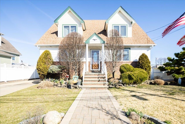 new england style home featuring roof with shingles, a front yard, and fence