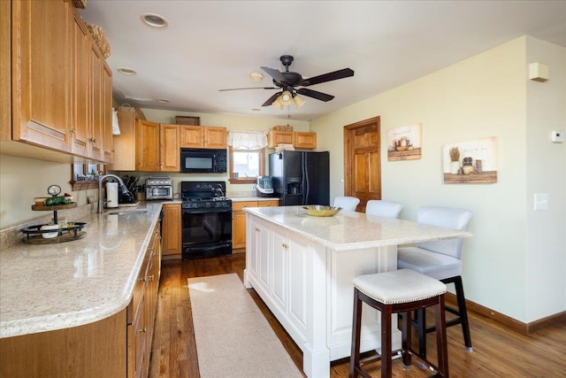 kitchen featuring a sink, a kitchen breakfast bar, a center island, black appliances, and ceiling fan