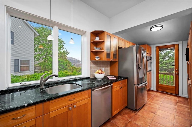 kitchen featuring hanging light fixtures, light tile patterned floors, a sink, brown cabinetry, and appliances with stainless steel finishes