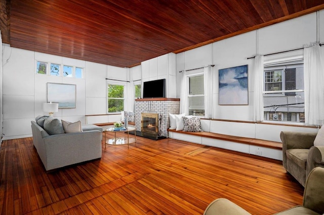 living area with a brick fireplace, a healthy amount of sunlight, wood-type flooring, and wooden ceiling