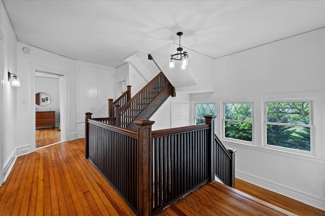 hallway featuring baseboards, hardwood / wood-style floors, an upstairs landing, and a chandelier