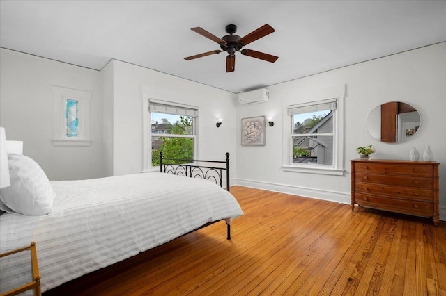 bedroom with an AC wall unit, baseboards, wood-type flooring, and multiple windows