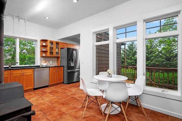 kitchen with brown cabinetry, backsplash, light tile patterned floors, dark countertops, and appliances with stainless steel finishes