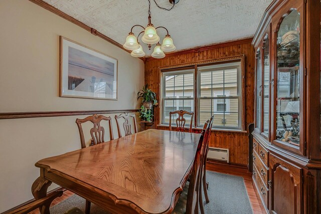 dining room with ornamental molding, a chandelier, wooden walls, a baseboard radiator, and wood finished floors
