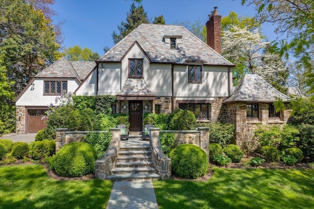 english style home with a chimney, a front yard, a high end roof, and stone siding