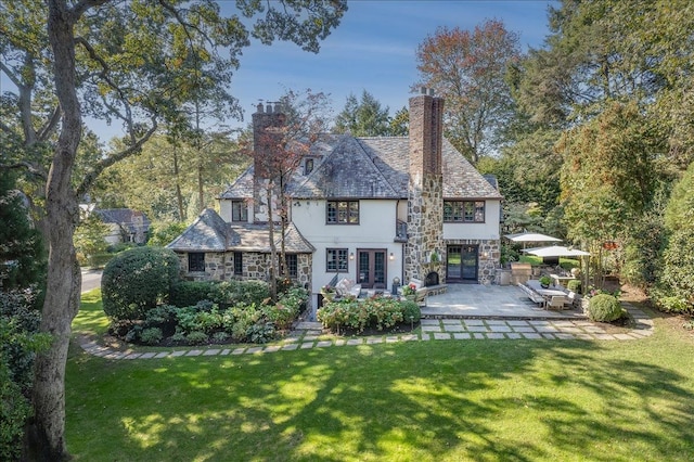 back of property featuring stucco siding, a chimney, a patio area, french doors, and a yard
