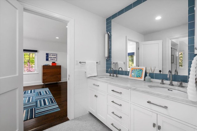 full bath with a sink, double vanity, recessed lighting, and wood finished floors