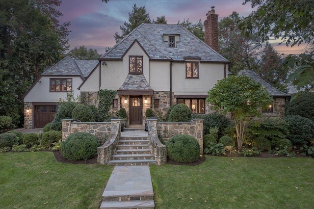 tudor home featuring a high end roof, a front yard, stone siding, stucco siding, and a chimney