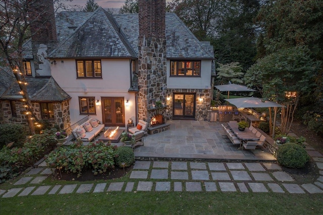 rear view of house with a high end roof, stone siding, stucco siding, a chimney, and a patio area
