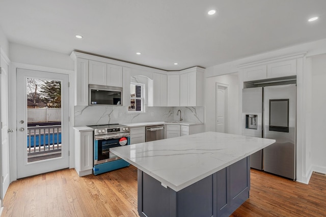 kitchen with backsplash, a sink, stainless steel appliances, white cabinets, and light wood-style floors