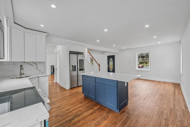 kitchen featuring white cabinetry, stainless steel refrigerator with ice dispenser, blue cabinets, backsplash, and a sink