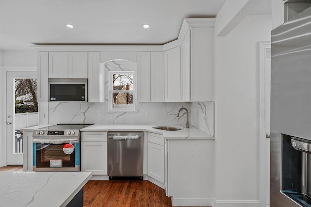 kitchen with light stone counters, white cabinets, a sink, and stainless steel appliances