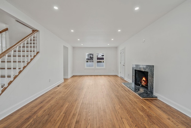 unfurnished living room featuring recessed lighting, a high end fireplace, wood finished floors, and stairway
