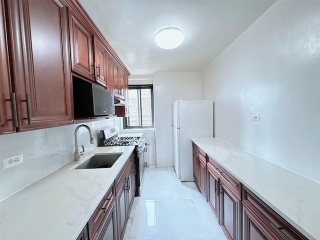 kitchen featuring stainless steel gas stove, backsplash, a sink, freestanding refrigerator, and light stone countertops