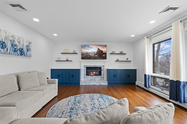 living room featuring a glass covered fireplace, wood finished floors, visible vents, and recessed lighting