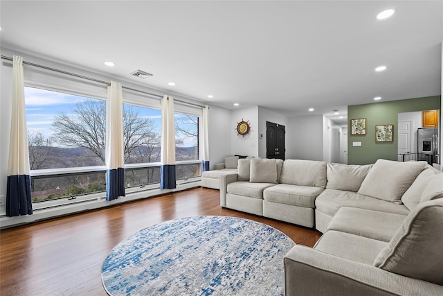 living area featuring a baseboard heating unit, wood finished floors, visible vents, and recessed lighting
