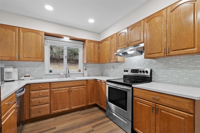 kitchen with a sink, under cabinet range hood, appliances with stainless steel finishes, light countertops, and dark wood-style flooring