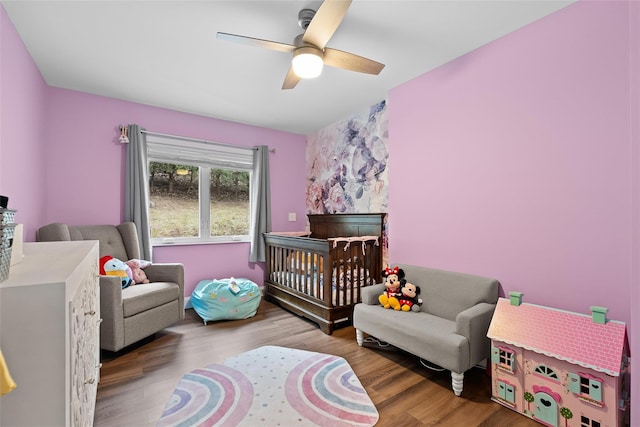 bedroom with a ceiling fan, wood finished floors, and a nursery area