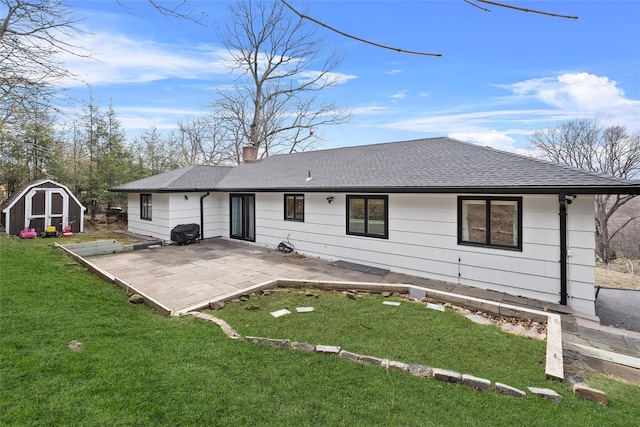 back of house featuring a chimney, a lawn, an outbuilding, a patio, and a storage unit
