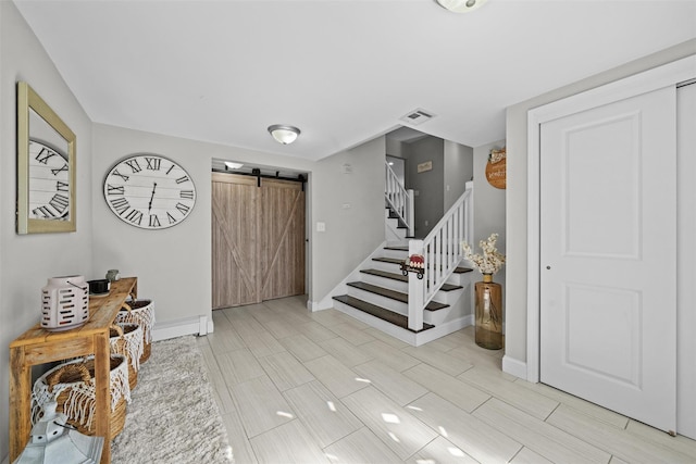 entrance foyer featuring stairway, a barn door, visible vents, and baseboards