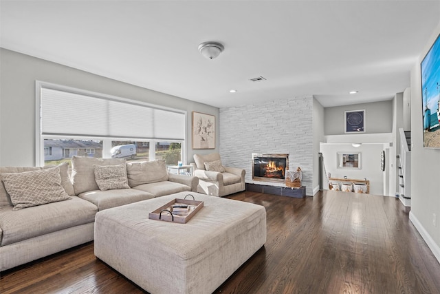 living room with dark wood-style flooring, visible vents, a stone fireplace, and recessed lighting