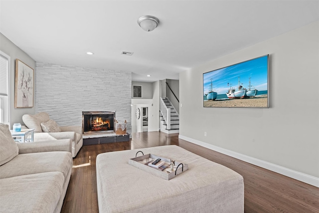living room with visible vents, a stone fireplace, wood finished floors, and stairs