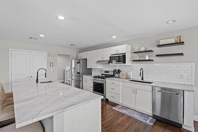 kitchen with under cabinet range hood, an island with sink, a sink, and appliances with stainless steel finishes