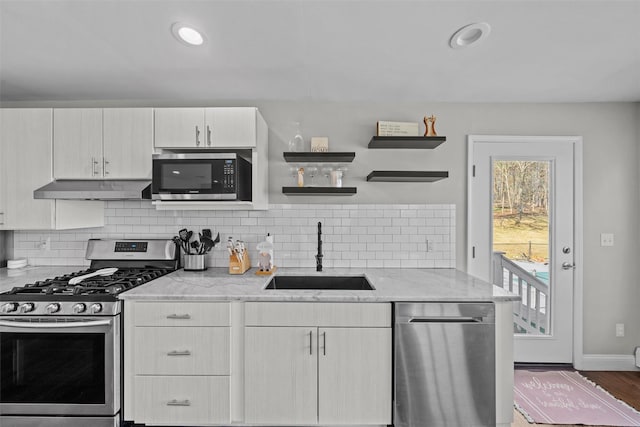 kitchen featuring light stone countertops, appliances with stainless steel finishes, under cabinet range hood, a sink, and backsplash