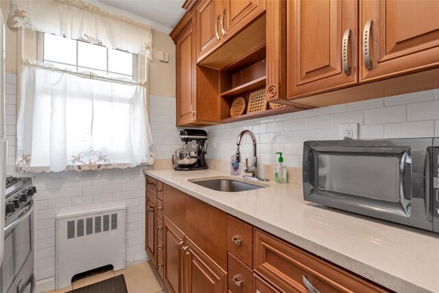kitchen featuring light countertops, brown cabinetry, stainless steel range oven, radiator, and a sink