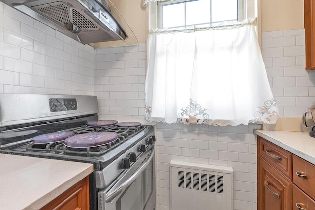 kitchen featuring radiator, exhaust hood, brown cabinetry, gas stove, and tile walls