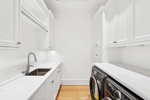 25 Fresh Pond Rd, North Haven, NY 11963 - clothes washing area with light wood finished floors, baseboards, cabinet space, a sink, and washing machine and dryer