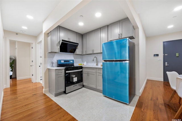 kitchen with gas range, range hood, gray cabinetry, a sink, and freestanding refrigerator