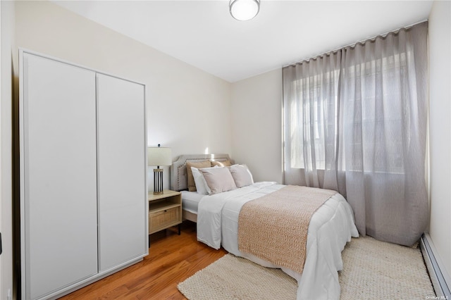 bedroom with a baseboard radiator, light wood-style flooring, and a closet