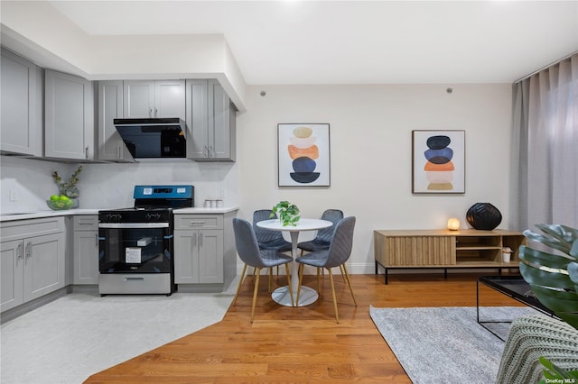 kitchen featuring light countertops, stainless steel gas stove, light wood finished floors, gray cabinetry, and decorative backsplash