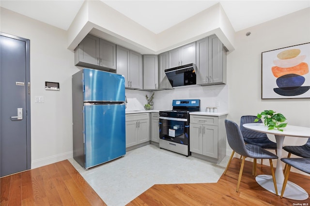 kitchen featuring light countertops, freestanding refrigerator, black microwave, gray cabinetry, and stainless steel gas range oven
