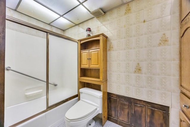 full bath with toilet, tile patterned floors, tile walls, visible vents, and bath / shower combo with glass door