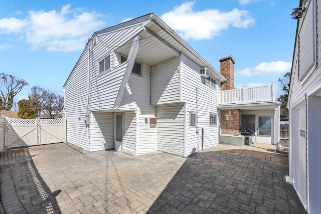 view of side of home with fence, an AC wall unit, a gate, a patio area, and a balcony