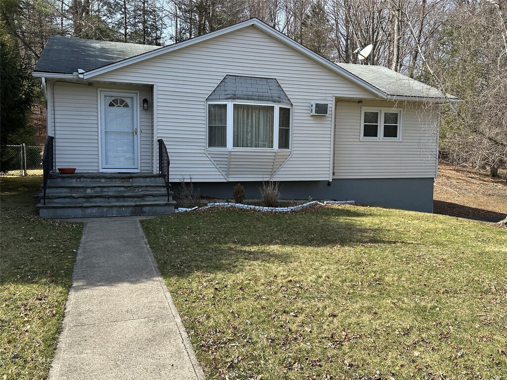 view of front of property featuring a front yard, fence, a shingled roof, entry steps, and an AC wall unit