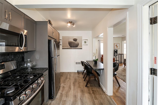 kitchen with radiator heating unit, appliances with stainless steel finishes, gray cabinetry, light wood-type flooring, and dark countertops