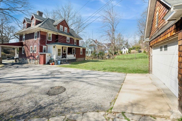 view of side of property featuring driveway, covered porch, a garage, a yard, and a chimney
