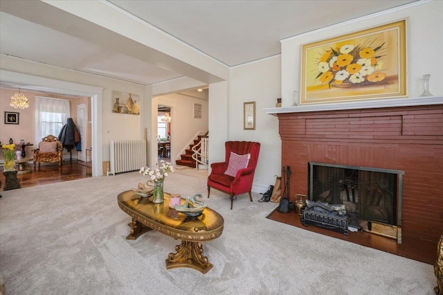 carpeted living area featuring a brick fireplace, radiator, crown molding, and stairs