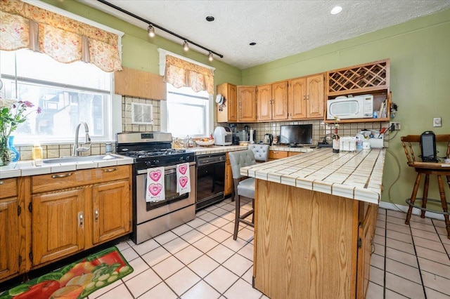 kitchen featuring decorative backsplash, a sink, stainless steel gas range, dishwasher, and white microwave