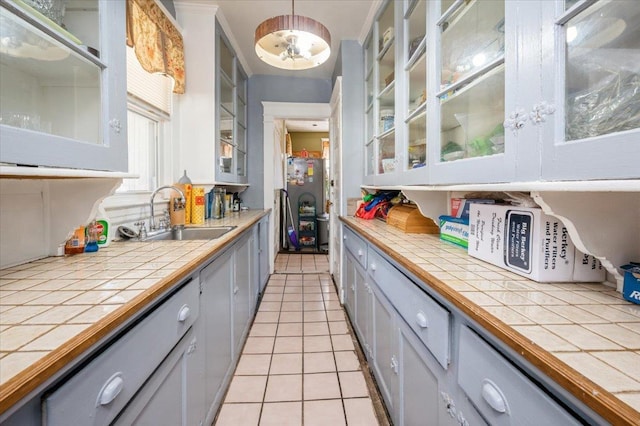 kitchen featuring stainless steel fridge, a sink, tile counters, and light tile patterned floors