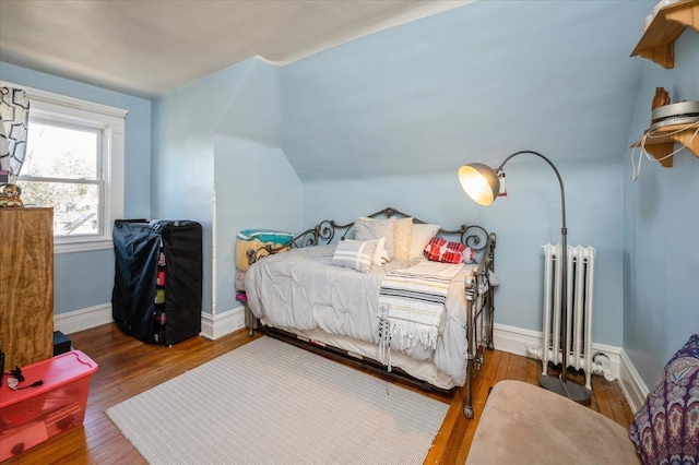 bedroom with baseboards, wood finished floors, vaulted ceiling, and radiator