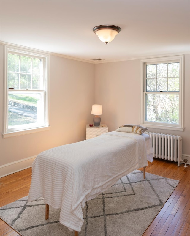 bedroom featuring visible vents, crown molding, hardwood / wood-style flooring, baseboards, and radiator