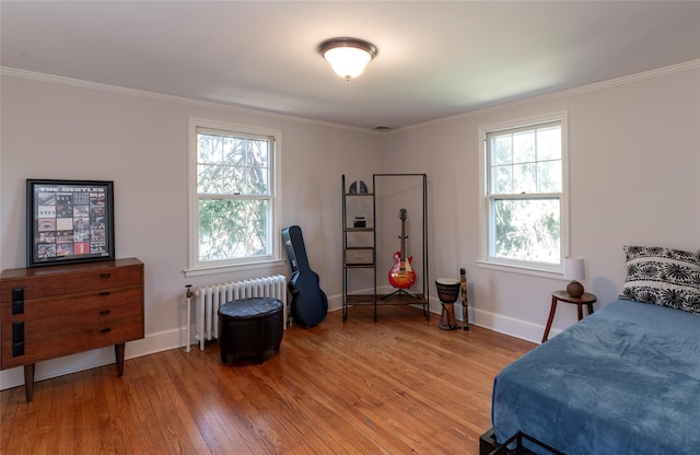 bedroom featuring visible vents, ornamental molding, baseboards, radiator heating unit, and light wood finished floors