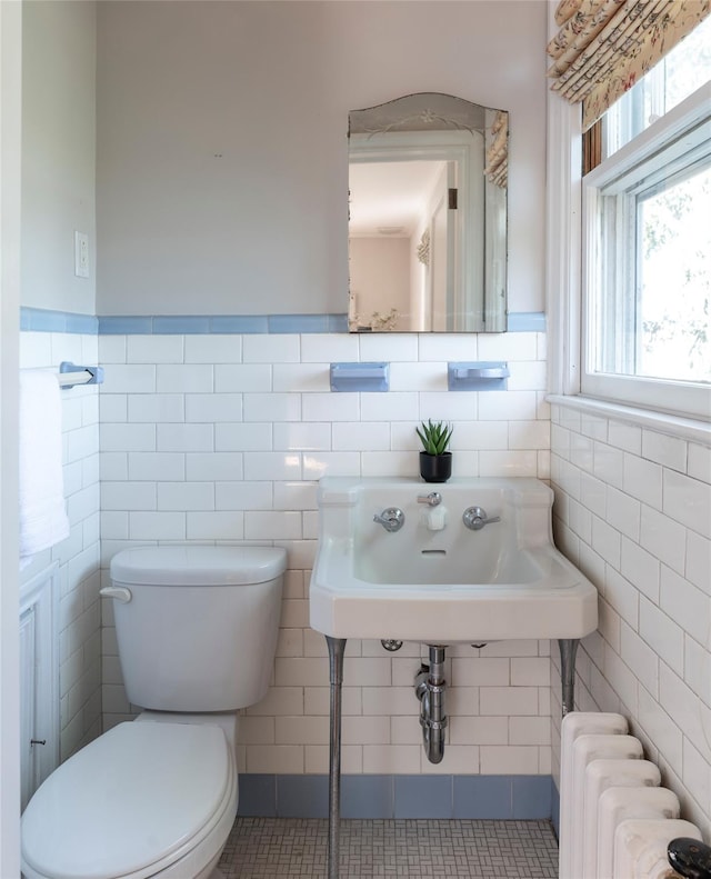 half bath with radiator, wainscoting, toilet, and tile walls