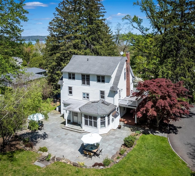rear view of property with a lawn, a shingled roof, a chimney, and a patio area