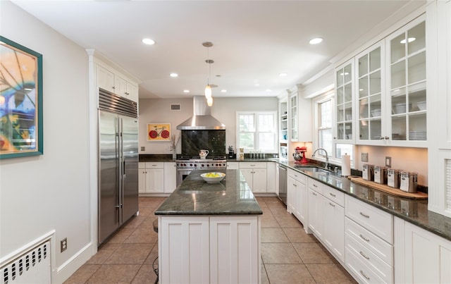 kitchen featuring wall chimney range hood, a sink, radiator, recessed lighting, and premium appliances