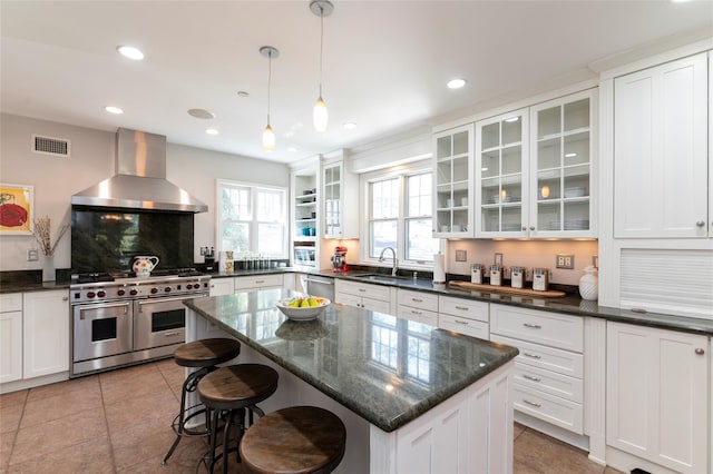 kitchen with a sink, a kitchen breakfast bar, wall chimney exhaust hood, double oven range, and visible vents